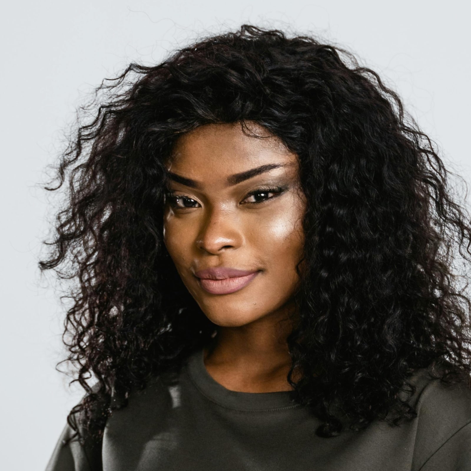 Portrait of a smiling woman with curly black hair wearing a dark gray top against a light background.